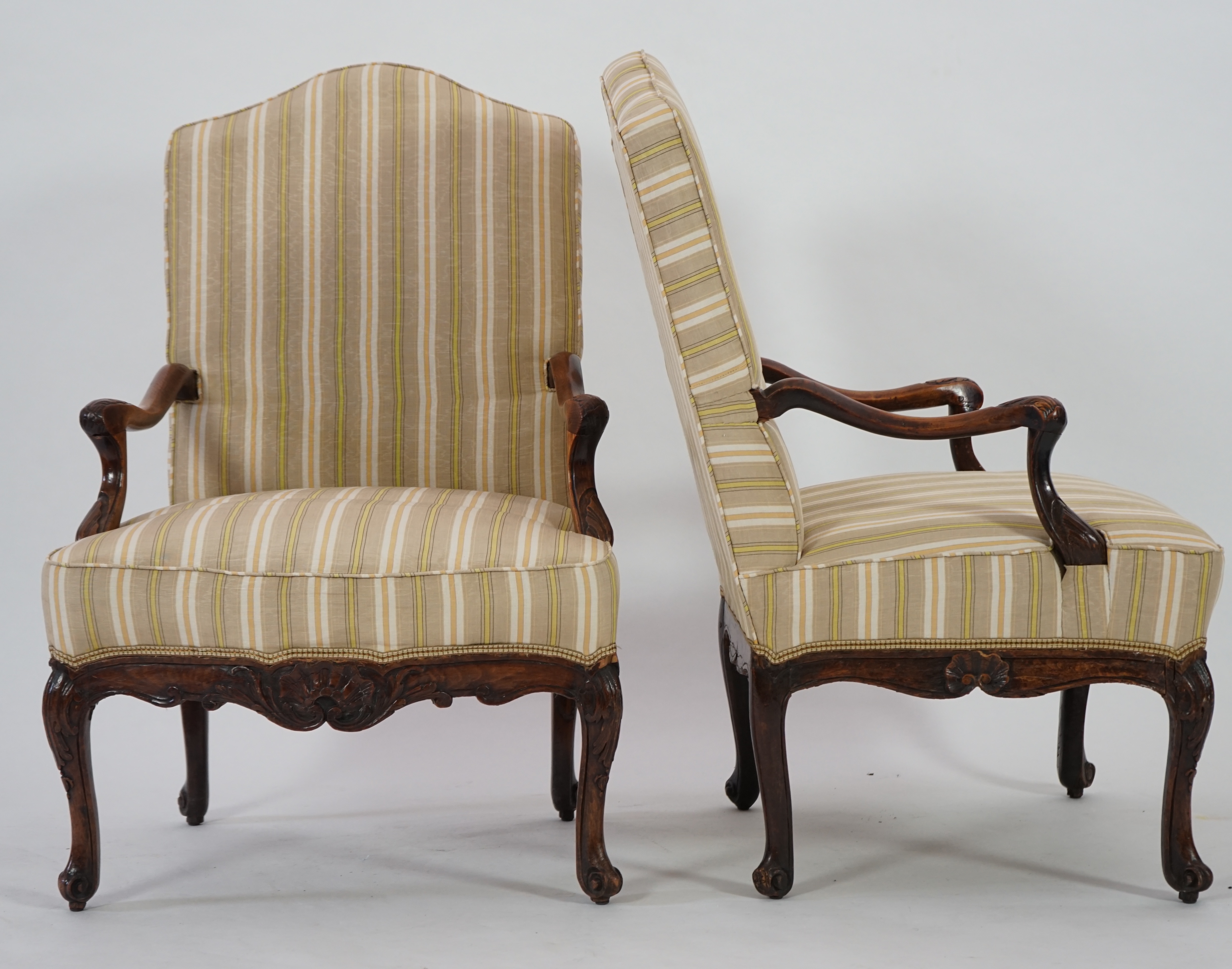 A pair of Louis XVI walnut fauteuils with upholstered backs and seats and foliate carved arms and underframes, on cabriole legs, width 67cm, depth 76cm, height 104cm. Condition - fair
